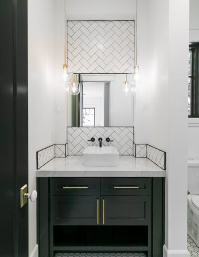 Modern bathroom with a white sink on a black vanity, herringbone tile backsplash, and two hanging pendant lights. Floor features hexagonal tiles.