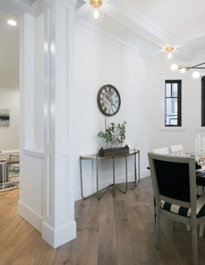 Open-concept living and dining area with modern decor. Features a dining table set for six, a wall clock, and large windows.