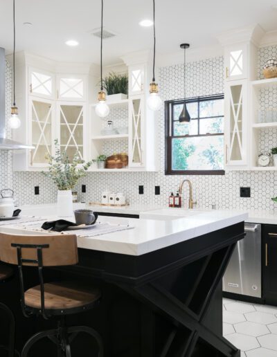 Modern kitchen with a large island, wooden stools, white cabinets, geometric backsplash, pendant lights, and stainless steel appliances.