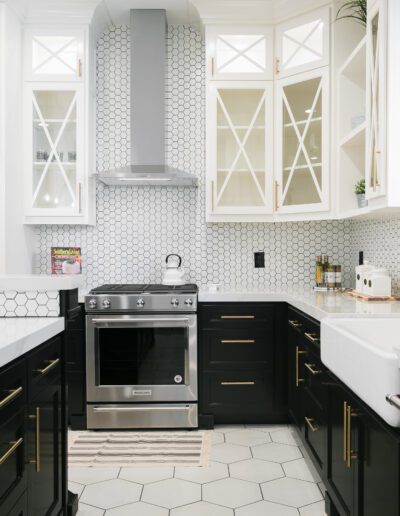 Modern kitchen with black and white cabinets, a stainless steel stove, hexagonal backsplash, and a farmhouse sink.