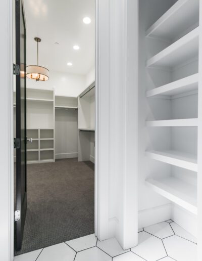 Empty walk-in closet with open shelves, carpeted floor, hexagonal tile at the entrance, and a ceiling light fixture.