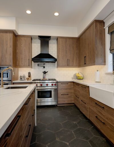 Modern kitchen with wooden cabinets, white countertops, stainless steel appliances, a farmhouse sink, and pendant lighting.
