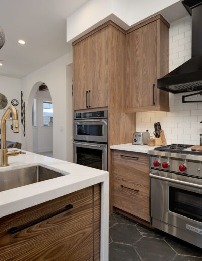 Modern kitchen with a large island, stainless steel appliances, wooden cabinets, and a black range hood. White subway tiles cover the backsplash.