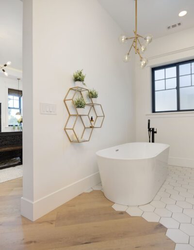 Modern bathroom with freestanding bathtub, hexagonal shelves, and adjacent view of a bedroom with a carved wooden bed.