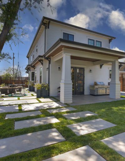 Two-story house with a white exterior, covered patio, and stepping stone pathway in a grassy backyard, surrounded by a wooden fence and trees.
