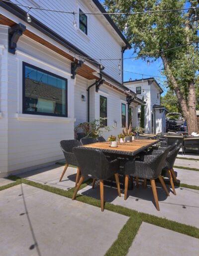 A modern backyard with a dining table, chairs, string lights, and a wooden privacy fence on a concrete patio.